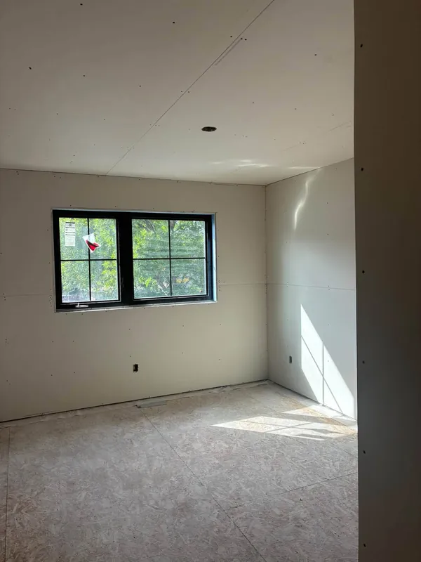 A room corner with new drywall, screws set and the ceiling joints visible before taping